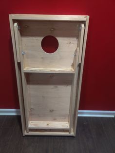 a wooden shelf with a hole in the middle and two shelves on each side, against a red wall