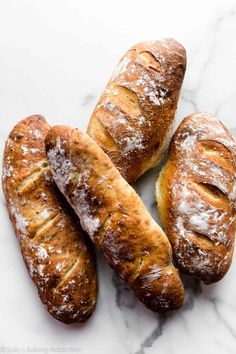 four loaves of bread sitting on top of a white marble counter with powdered sugar