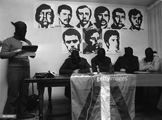 people sitting at desks with faces on the wall in front of them and one person standing