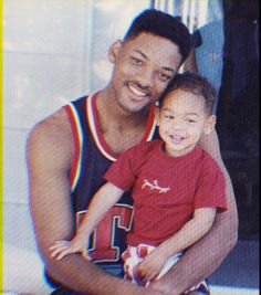 a man holding a small child in his arms and smiling at the camera with another person behind him