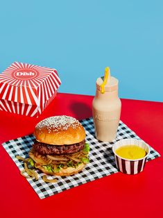 a hamburger and fries on a table next to a cup of mustard, ketchup and a drink