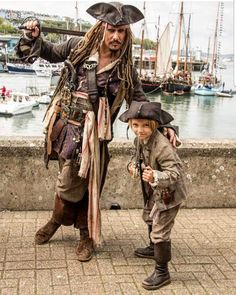 a little boy standing next to a man in pirate costume