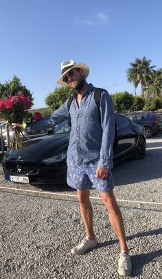 a man standing in front of a car wearing a cowboy hat and blue dress shirt