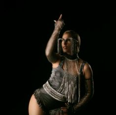 a woman in black and silver outfit posing for the camera with her hand up to her head