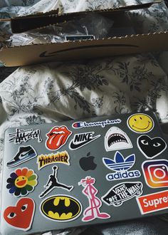 an open laptop computer sitting on top of a bed covered in stickers and decals