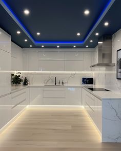 a modern kitchen with white cabinets and marble counter tops is illuminated by blue lighting from the ceiling