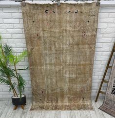 an old rug hanging on a brick wall next to a potted plant and ladder