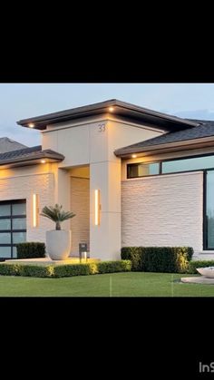 a modern house is shown at night with lights on the windows and grass in front