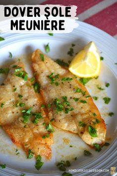 two pieces of fish on a white plate with lemon wedges and parsley garnish