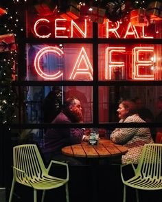 two people sitting at a table in front of a neon sign that says central cafe