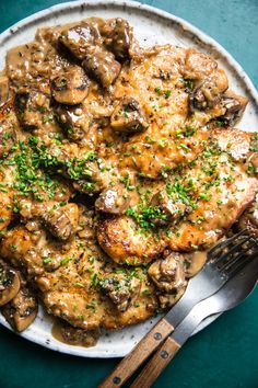 a white plate topped with meat covered in mushroom gravy next to a fork