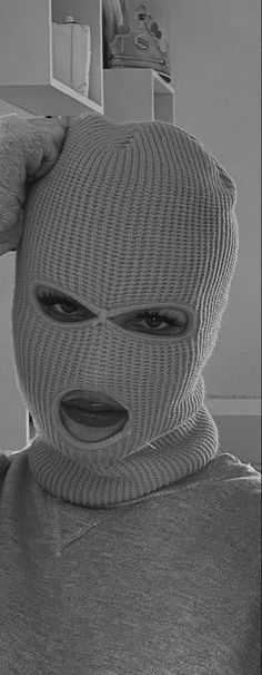 black and white photograph of a person wearing a knitted mask with one hand on their head