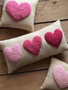 three pillows with pink hearts on them sitting on a wooden floor next to each other