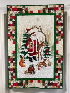 This is a charming scene of Santa standing in a woodland with deer, rabbits and birds in the center fabric panel. Evergreen trees and snowflakes complete this serene setting.   The panel is surrounded with a pieced border featuring Christmas prints and then bound in a coordinating green fabric.  There is a hanging sleeve across the top back to accommodate a rod for easy hanging. This could also be used for a holiday lap quilt too. It measures 33" x 38." Quilt With Panel, Christmas Fabric Panels, Quilt Wall Hangings, Christmas Quilt Ideas, Panel Quilt Patterns, Quilt Borders, Christmas Wall Hangings, Quilt Wall, Christmas Journal