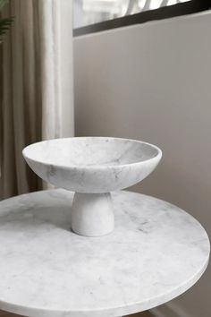 a white marble table with a bowl on it's top next to a window