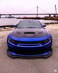 a blue car parked in front of a large body of water with a bridge in the background