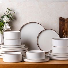 white dishes are stacked on top of each other in front of a vase with flowers