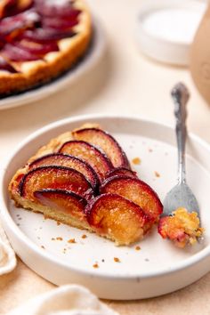 a slice of pie on a plate with a fork next to it and another dessert in the background