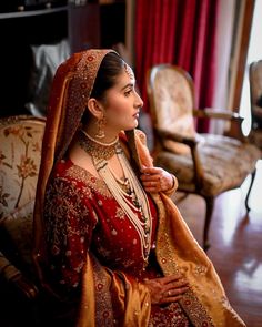 a woman in a red and gold bridal gown sitting on a couch with her hand on her shoulder