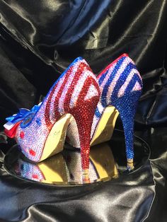 two colorful high heel shoes sitting on top of a black cloth covered surface, one with red, white and blue sequins