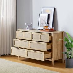 a wooden dresser with three drawers next to a potted plant and framed pictures on the wall