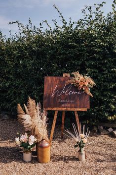 a welcome sign with flowers and plants in vases on the ground next to it