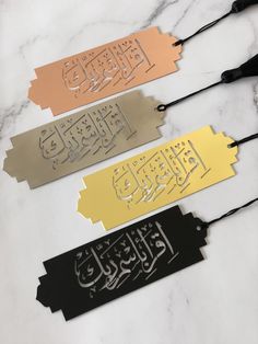 three metal name tags with arabic calligraphy on them sitting on a marble countertop