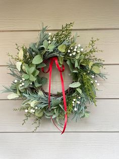 a christmas wreath hanging on the side of a house with a red ribbon around it