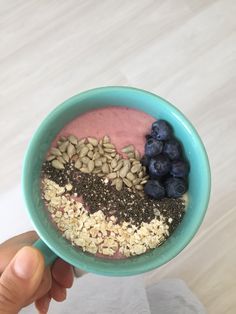 a person holding a bowl of food with berries and oatmeal in it