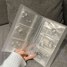 a person is holding an open plastic case with various jewelry items in it on a couch