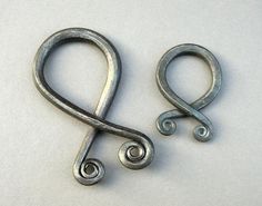 two metal hooks on a white surface one is shaped like an amp clef and the other has a spiral design