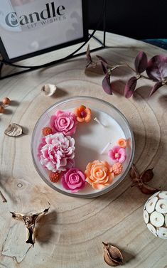 a cake decorated with pink and orange flowers on a wooden table next to some candles