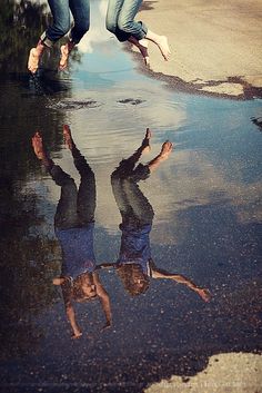 two people jumping in the air with their reflection on the wet pavement and puddles