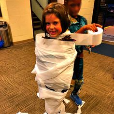 two children are playing with toilet paper on the floor while one girl is holding a roll of toilet paper