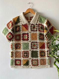 a crocheted sweater hanging on a wooden hanger next to a potted plant