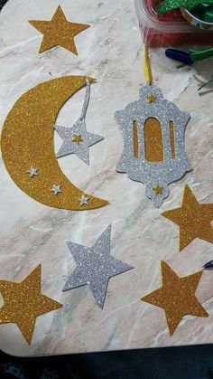 some gold and silver glittered stars on a table with a crescent, lantern and star ornament