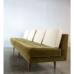 a green couch with three pillows on it's back and two legs, in front of a white wall