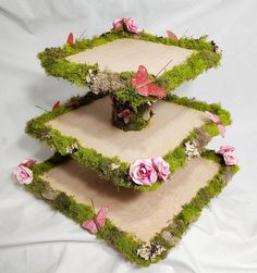 three tiered trays with pink flowers and grass on the bottom one is made out of wood