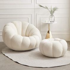 two white chairs and a table with a plant in it on a rug next to a wall