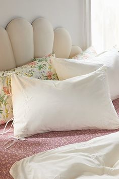 four pillows on a bed with white headboard and pink bedspread in the background