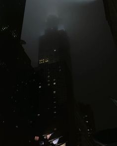 a dark city at night with the lights on and skyscrapers lit up in the fog