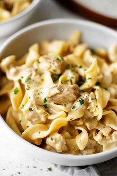 a white bowl filled with pasta covered in sauce and parsley on top of a table