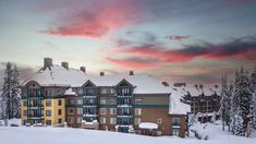 an apartment building with snow on the ground and trees in front of it at sunset