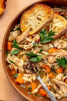 a bowl filled with chicken and vegetable soup next to slices of bread on the side