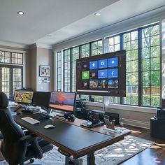 there are many computers on the desk in this office space with large windows that look out onto the yard