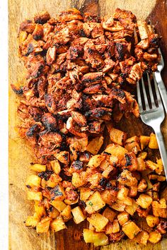 a wooden cutting board topped with chicken and potatoes next to a fork on top of it