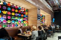 people sitting at tables in a restaurant with colorful lights hanging from the wall behind them