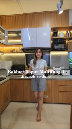 a woman standing in the middle of a kitchen next to a stove top oven and microwave