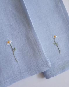 two daisies embroidered on the side of a light blue linen shirt with white piping