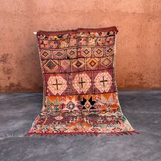 an old rug is laying on the floor in front of a wall with a cross design